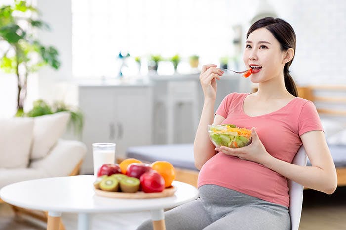 A pregnant woman eats her lunch of salad fresh fruit and a glass of milk