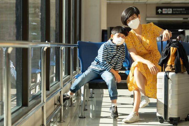 A woman and her son wearing face masks, waiting in the airport lounge
