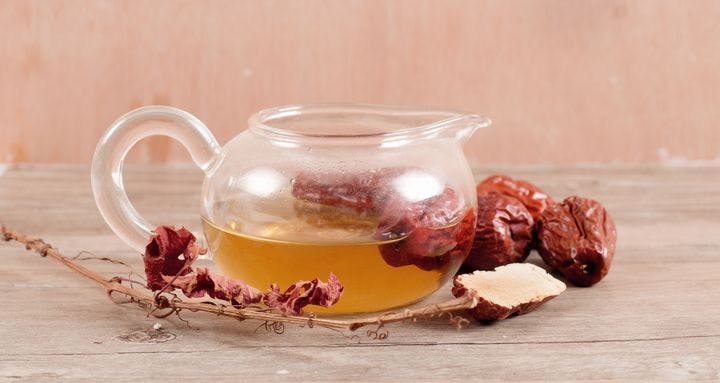 Jujubes and tea inside a clear teacup on a wooden background