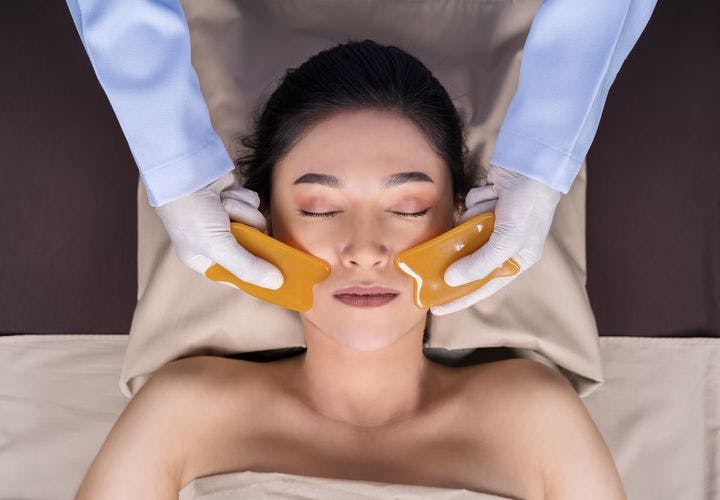 A woman getting a gua sha facial massage at a salon