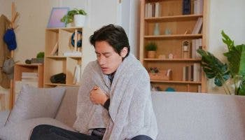 Sick Asian man covered in a blanket having fever with chills.