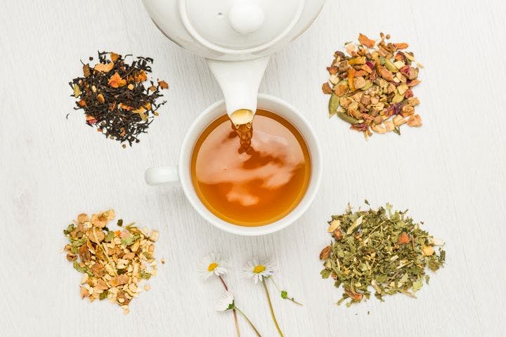 Photo of herbal tisane being poured out of teapot with herbs on the side