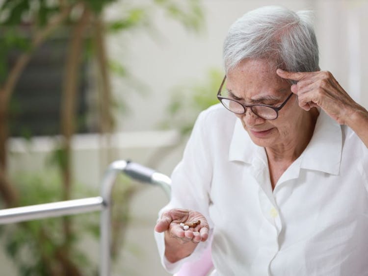 Elderly woman looking at pills in her hand and seeming confused