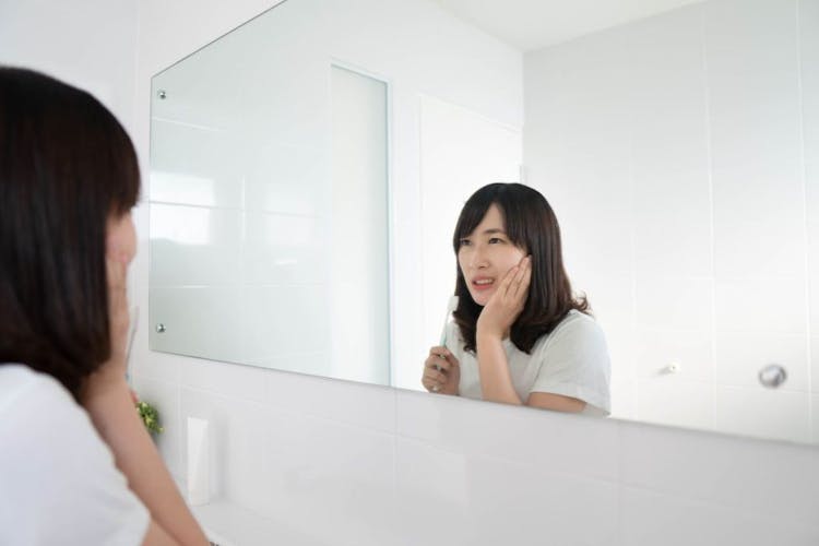 An Asian woman suffering from a toothache while brushing her teeth in front of the bathroom mirror. 