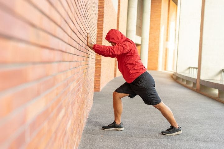 Man looking down as he performs stretches against a red brick wall. 