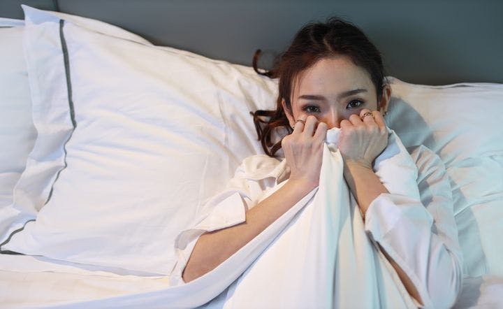 Woman in bed, covering the bottom half of her face with a blanket.