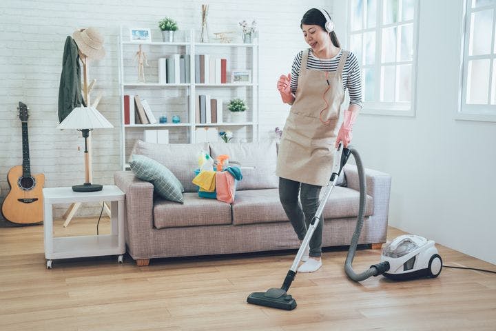 Woman with headphones dancing while using a vacuum to clean a wooden floor