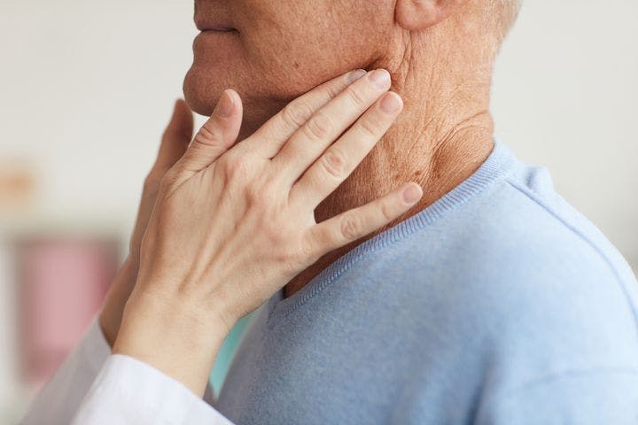 Healthcare practitioner examines the sides of an elderly patient’s neck using her hands.