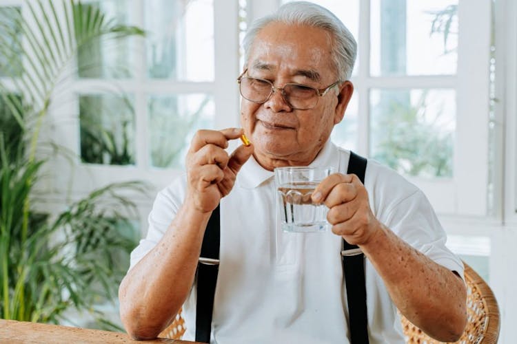 Senior Asian man with cup of water and pill