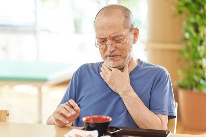 A man in old age holds his throat, having difficulty swallowing while eating.