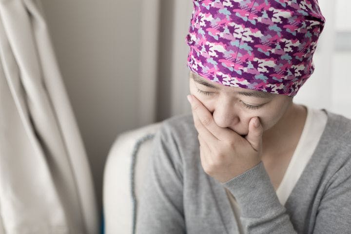 Woman wearing a headwrap covering her mouth and looking ill. 
