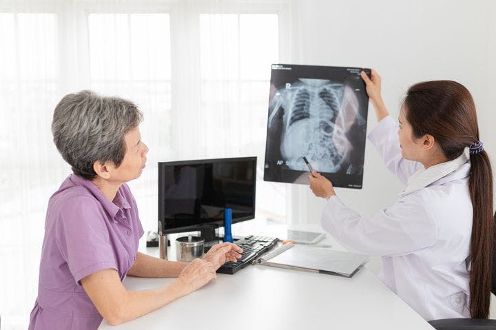 A woman looking on as a clinical specialist explains the findings of an X-ray image to her.