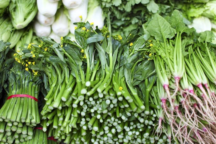 Leafy green vegetables piled up on each other with roots visible. 