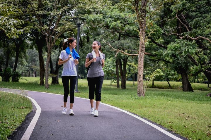 Two women smiling at each other as they walk side-by-side on a park pathway. 