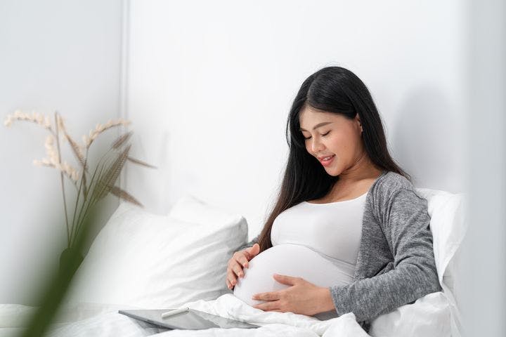 Pregnant woman in bed smiling and looking at her baby bump.