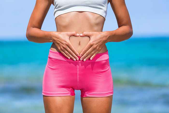 A woman forms a heart shape with her hands and places her hands on top of her stomach