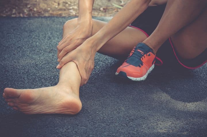 Woman sitting on the ground and holding her right shin area with both hands