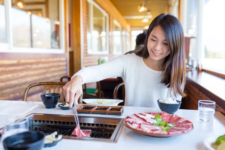 Woman using a pair of tongs to place meat on a grill