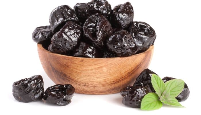 Smoked plums (Wu Mei) with a mint leaf in wooden bowl isolated on white background.