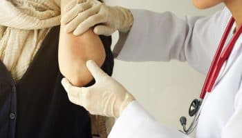 A dermatologist inspects a patch of red skin on the forearm of an eczema patient.