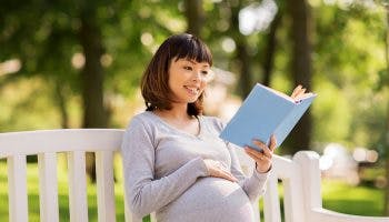 A pregnant woman sits in a park reading a book