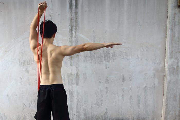 A shirtless man using a resistance band to perform a shoulder exercise