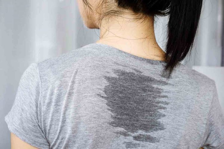 A close-up shot of an Asian woman’s back, with sweat stains on the back of her T-shirt