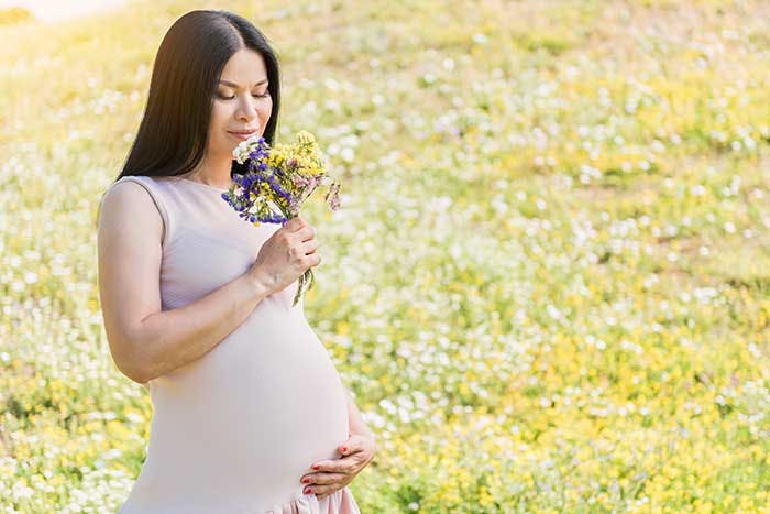 A pregnant woman holding her belly and smelling a bouquet of flowers