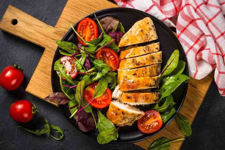 Grilled chicken fillet with fresh salad on a black plate placed on top of a wooden tray