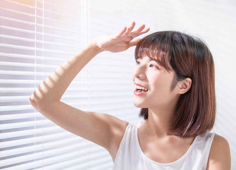 Woman reacting happily to sun exposure from her window blinds