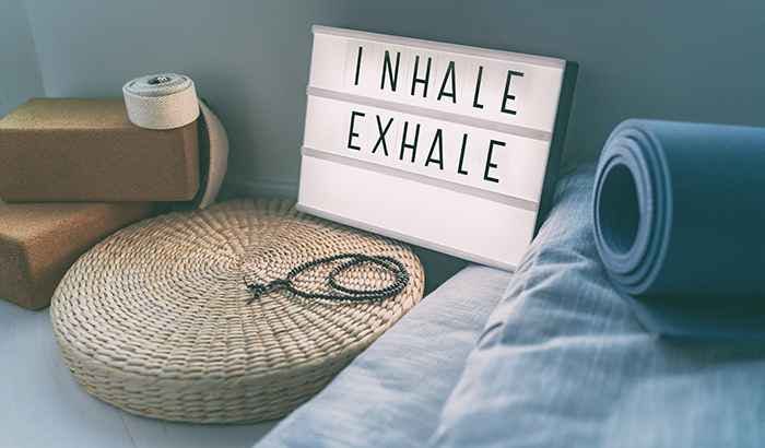 A rattan cushion, two yoga blocks, blue mattresses, and a sign says “Inhale/Exhale”