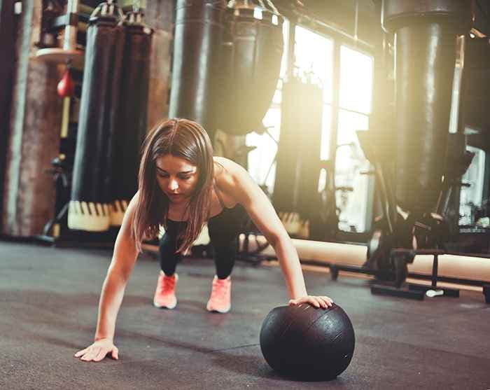 A slim-figured female practising plank with a medicine ball in a gym