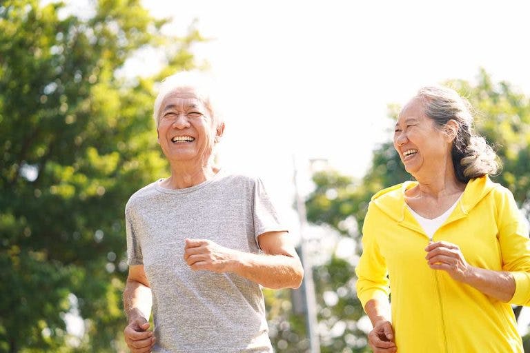 An elderly Asian couple running outdoors with smiles on their faces