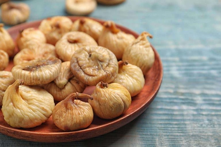 Dried figs on a wooden plate and on a wooden table