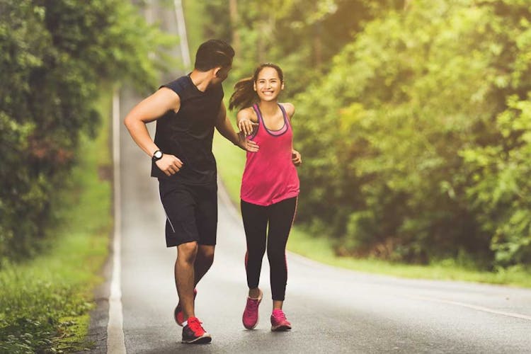 A man in sports clothes extends a helping hand to a woman as they jog on a downhill road