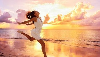 A girl in a white dress jumping joyfully on the beach during a sunset