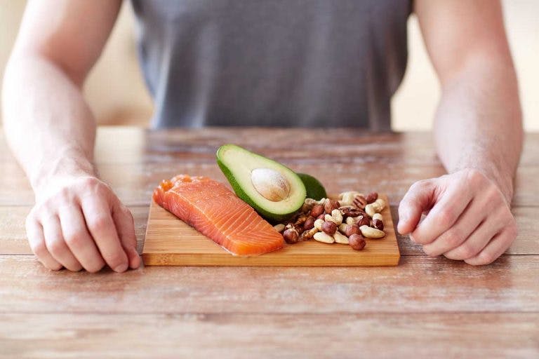 A closeup of man in front of a portion of raw salmon, avocado, and almond nuts