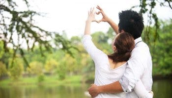 A couple forming the shape of a heart with their fingers at a lakeside