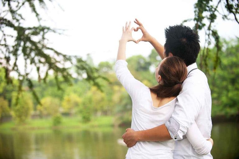 A couple forming the shape of a heart with their fingers at a lakeside
