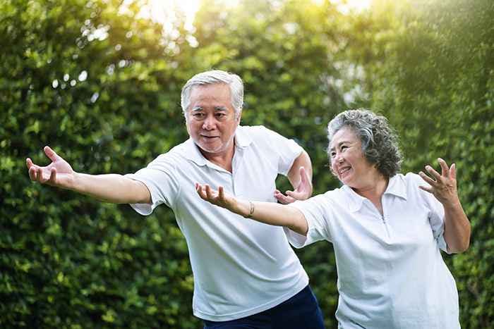 Elderly Asian couple practising tai chi together outdoors