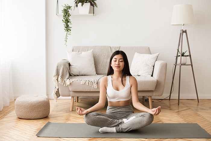 A woman in sportswear meditating on a grey yoga mat in an empty room