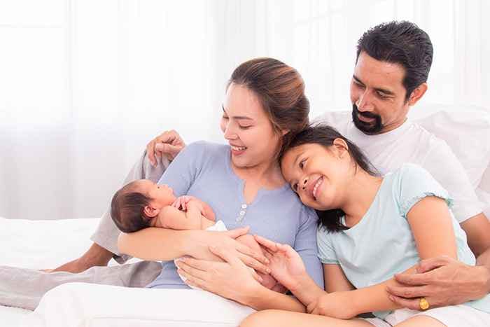 A family huddled together as they look lovingly at a newborn baby being held in the mother’s arms