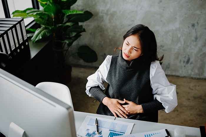 A female employee sitting in front of a computer while holding her stomach with a painful expression