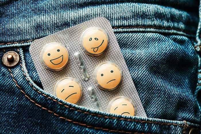 Orange pills kept in jeans pocket with different mood expressions drawn on them