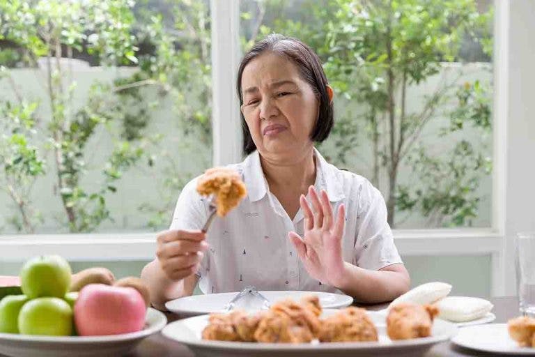 Senior Asian woman holds a fried chicken but shows her lack of appetite