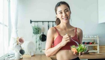 Young attractive Asian woman eating a healthy bowl of salad in her kitchen