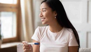 A young Asian woman smiles while holding pregnancy test result