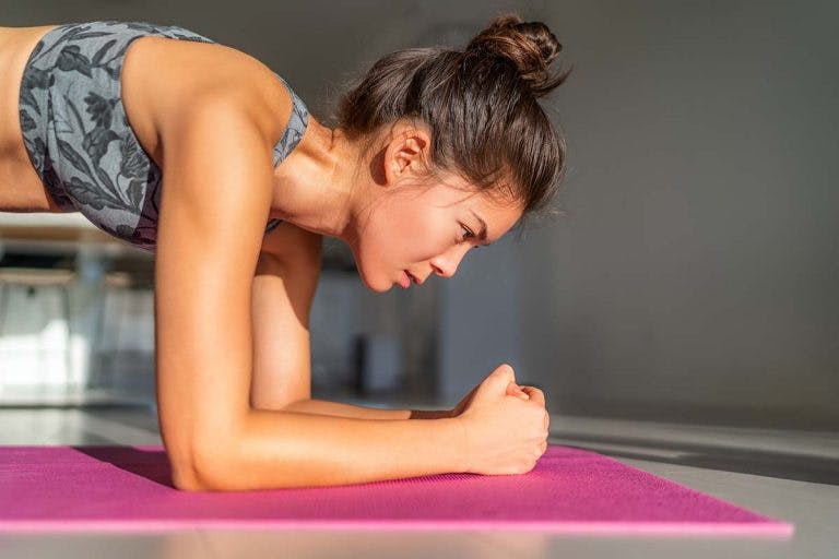 Woman doing an elbow plank exercise on a purple yoga mat