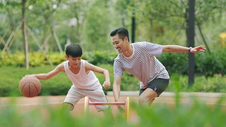 Father and son playing basketball at an outdoor court. 