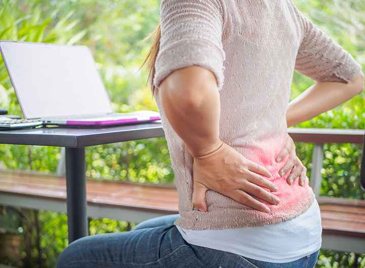 Woman holding her lower back in pain while sitting down